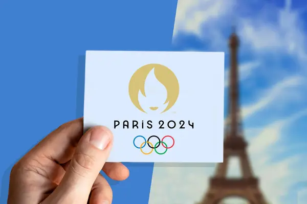 Paris Olimpiyatları 2024 logosu kule arka planında bulanık duran kağıt üzerinde sergileniyor.