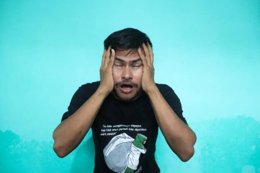 Tecrit edilmiş yeşil arka planda yakışıklı Asyalı genç adam bazı ifadeler yapıyor. Bunu yaparken rahat görünüyor.