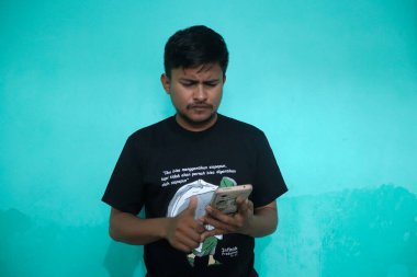 Tecrit edilmiş yeşil arka planda yakışıklı Asyalı genç adam bazı ifadeler yapıyor. Bunu yaparken rahat görünüyor.