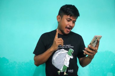 Tecrit edilmiş yeşil arka planda yakışıklı Asyalı genç adam bazı ifadeler yapıyor. Bunu yaparken rahat görünüyor.