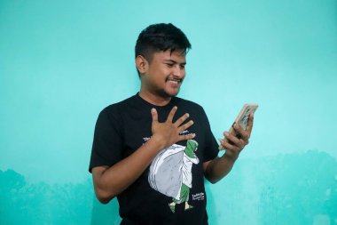 Tecrit edilmiş yeşil arka planda yakışıklı Asyalı genç adam bazı ifadeler yapıyor. Bunu yaparken rahat görünüyor.