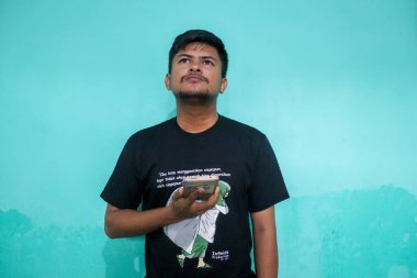 Tecrit edilmiş yeşil arka planda yakışıklı Asyalı genç adam bazı ifadeler yapıyor. Bunu yaparken rahat görünüyor.