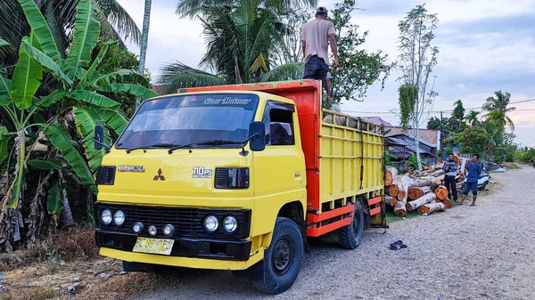 Aceh, Endonezya 26 Mart 2023: Asyalı çalışkan adamlar nakliye kamyonlarından kirişleri indiriyor. Kuzey Aceh, Aceh Eyaleti, Endonezya 26 Mart 2023