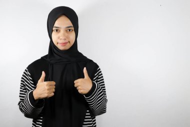 Asyalı genç Müslüman kadın başparmağı yukarıda beyaz arka planda izole edilmiş.