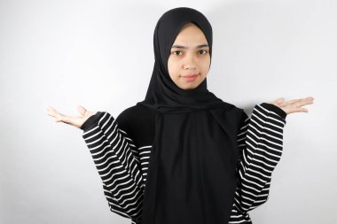 Asyalı genç Müslüman kadın portresi beyaz arka planda el hareketi ile tesettüre bürünmüş.