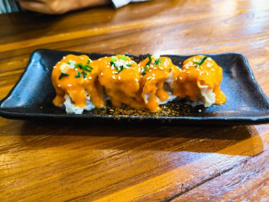 Somon balıklı suşi ruloları ve ahşap tabakta peynir.