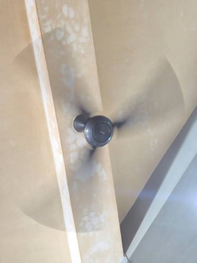 Modern bir tavan vantilatörü yüksek hızda döner, açık renkli, desenli iç tavan üzerinde bulanık gölgeler bırakır. Hareket eden vantilatör odada bir soğutma etkisi yaratıyor..