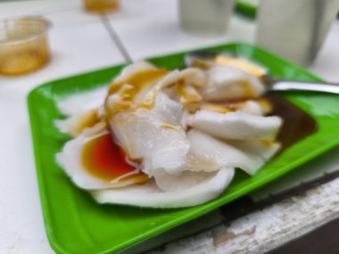 Tatlı karamel ve kırmızı meyve sosu serpiştirilmiş, canlı yeşil bir tabakta servis edilen, buğulanmış pirinç rulolarının yakın plan görüntüsü..