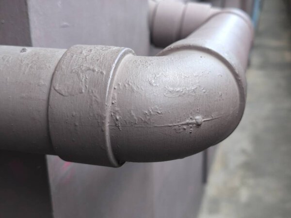 Вид крупным планом подчеркивает соединение промышленных труб с локтевым шарниром и текстурированной светло-коричневой окрашенной поверхностью..