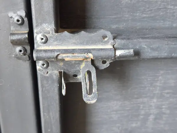 Eski, paslı, siyah metal bir kapının sürgüsünü ve karanlık bir yüzeye sürgüsünü yakından çek. Yıpranmış donanım yaşı gösteriyor ve güvenli, endüstriyel bir görünüm sağlıyor..