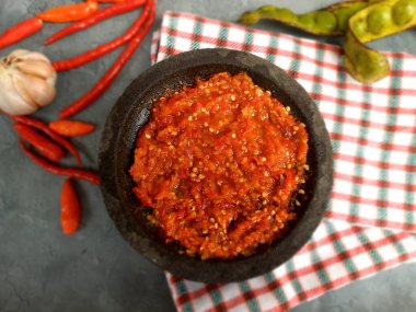 Fresh sambal served on stone mortar (cobek) with chili pepper and napkins backround. Sambal is traditional sauce from indonesia made from chili.