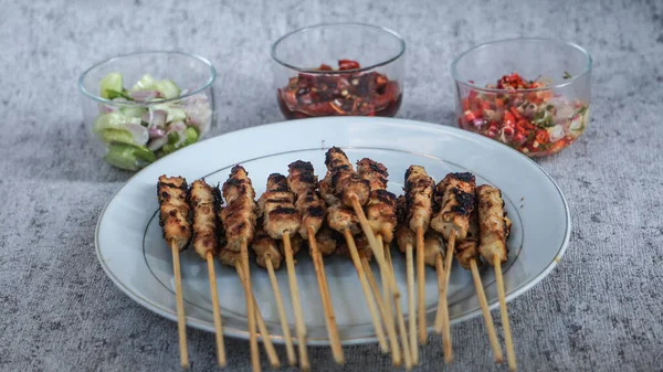 Beyaz tabakta satay pilav, turşu, soya sosu ve sambal matah ile servis edilir. Tazeliği aşikar. yan görünüm