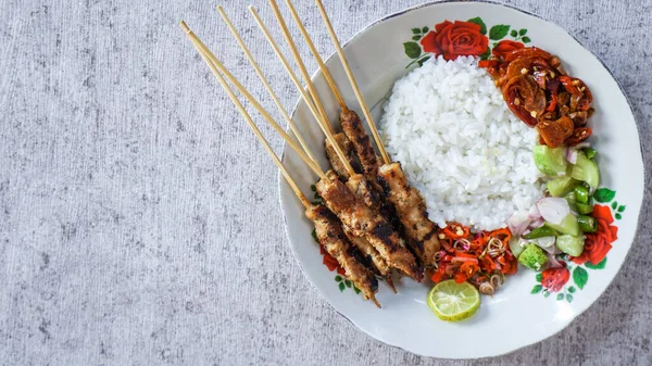 Beyaz tabakta satay pilav, turşu, soya sosu ve sambal matah ile servis edilir. Tazeliği aşikar. Üst görünüm hizalaması
