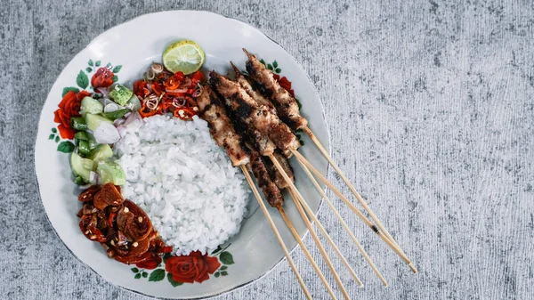 Beyaz tabakta satay pilav, turşu, soya sosu ve sambal matah ile servis edilir. Tazeliği aşikar. Üst görünüm sol hiza