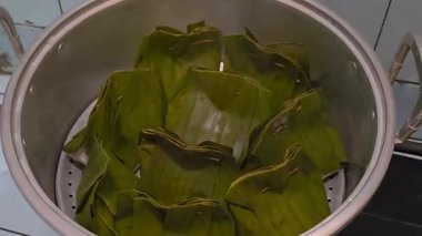 Geleneksel tariflerle dolu eko muz yaprağı yiyecek paketleri paslanmaz çelik bir tencerede buğulanıyor.