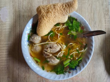 Tahta masada servis edilen kraker ve sebzeli geleneksel Endonezya köftesi çorbası.