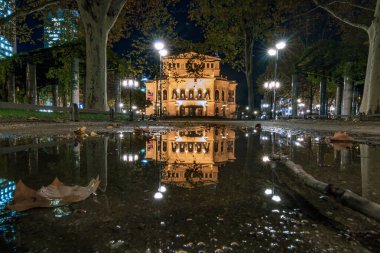 Akşam Frankfurt 'ta Alte Oper var. Almanya 'daki tarihi binanın mavi saatindeki güzel fotoğrafı. Sonbahar yağmuru ve ıslak toprak