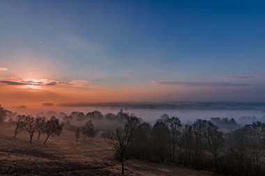 Güneşin doğuşunu gören bir kumtaşı kayası ve vadide sis var.