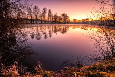 Almanya 'da bir gölün üzerinde gün batımı güzel bir gün doğumu. Sakin sularda ve güzel yeşil doğada bir yansıma.