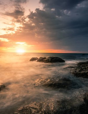 Fuerteventura Kanarya Adaları 'nda gün doğumu veya batımı. Sahilde, taşlarla ve uzun pozlarla. Eşsiz ışık. Saf tatil hissi. ince bulutlar