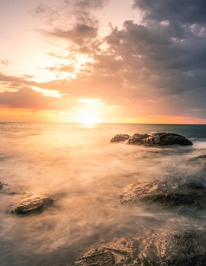 Fuerteventura Kanarya Adaları 'nda gün doğumu veya batımı. Sahilde, taşlarla ve uzun pozlarla. Eşsiz ışık. Saf tatil hissi. ince bulutlar