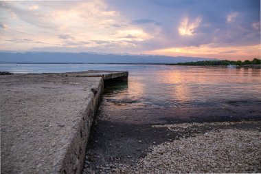 Beach in the morning. Sunrise, pebble beach on a rocky coast. The sky is reflected in the water of a bay. Natural spectacle of a Mediterranean landscape, island of Vir, Zadar, Dalmatia, Croatia, Adria clipart