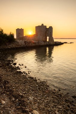 Rocky Sahili 'nde gün doğumu. Sakin sudaki yansıma. Akdeniz 'deki Kastelina Kalesi, Vir, Dalmaçya, Hırvatistan ve Adriyatik Denizi' nin yenilenmiş kalıntılarının manzara görüntüsü