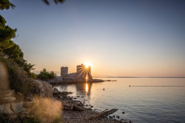 Şafak vakti kale harabeye döner. Akdeniz 'de güneş doğarken sakin sularla dolu bir körfez. Kastelina Kalesi, Vir Adası, Zadar, Dalmaçya, Hırvatistan, Adriyatik Denizi 'nin Gökyüzü ve Akdeniz manzarasının yansıması