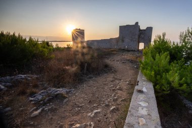 Rocky Sahili 'nde gün doğumu. Sakin sudaki yansıma. Akdeniz 'deki Kastelina Kalesi, Vir, Dalmaçya, Hırvatistan ve Adriyatik Denizi' nin yenilenmiş kalıntılarının manzara görüntüsü