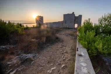 Rocky Sahili 'nde gün doğumu. Sakin sudaki yansıma. Akdeniz 'deki Kastelina Kalesi, Vir, Dalmaçya, Hırvatistan ve Adriyatik Denizi' nin yenilenmiş kalıntılarının manzara görüntüsü