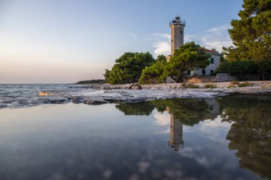 Kayalık bir sahilde, deniz feneri ve çam ormanıyla güzel bir gün batımı. Akdeniz, Vir, Dalmazien, Hırvatistan ve Adriyatik 'teki sahil şeridine bakın.