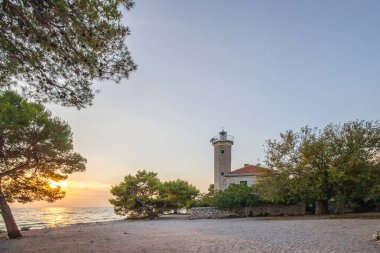 Kayalık bir sahilde, deniz feneri ve çam ormanıyla güzel bir gün batımı. Akdeniz, Vir, Dalmazien, Hırvatistan ve Adriyatik 'teki sahil şeridine bakın.