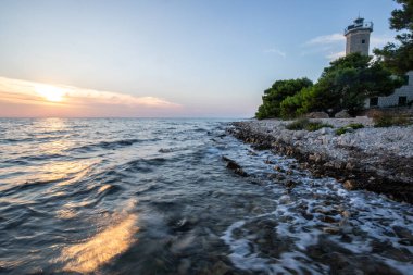 Kayalık bir sahilde, deniz feneri ve çam ormanıyla güzel bir gün batımı. Akdeniz, Vir, Dalmazien, Hırvatistan ve Adriyatik 'teki sahil şeridine bakın.