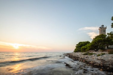 Kayalık bir sahilde, deniz feneri ve çam ormanıyla güzel bir gün batımı. Akdeniz, Vir, Dalmazien, Hırvatistan ve Adriyatik 'teki sahil şeridine bakın.