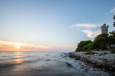 Kayalık bir sahilde, deniz feneri ve çam ormanıyla güzel bir gün batımı. Akdeniz, Vir, Dalmazien, Hırvatistan ve Adriyatik 'teki sahil şeridine bakın.