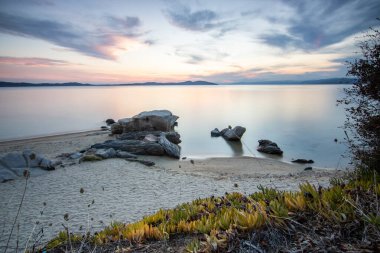 View through rocks on a sandy beach into the sunset. Landscape shot with a view to the horizon over the wide sea on the coast of Ouranoupoli, Thessaloniki, Central Macedonia, Greece clipart