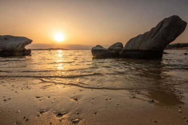 Kumlu bir sahildeki kayaların arasından gün batımına bak. Manzara, Ouranoupoli, Selanik, Orta Makedonya ve Yunanistan kıyılarındaki engin deniz manzarası ile çekildi