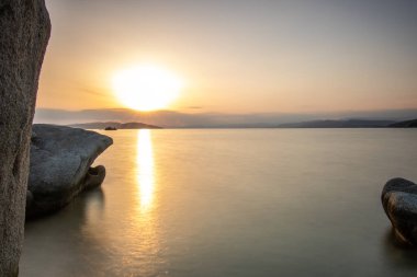 View through rocks on a sandy beach into the sunset. Landscape shot with a view to the horizon over the wide sea on the coast of Ouranoupoli, Thessaloniki, Central Macedonia, Greece clipart