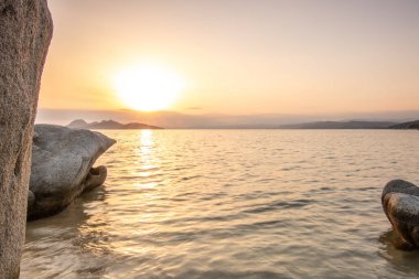 Kumlu bir sahildeki kayaların arasından gün batımına bak. Manzara, Ouranoupoli, Selanik, Orta Makedonya ve Yunanistan kıyılarındaki engin deniz manzarası ile çekildi