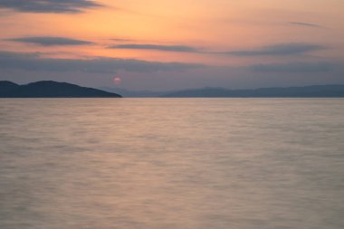 Kumlu bir sahildeki kayaların arasından gün batımına bak. Manzara, Ouranoupoli, Selanik, Orta Makedonya ve Yunanistan kıyılarındaki engin deniz manzarası ile çekildi