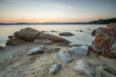 View through rocks on a sandy beach into the sunset. Landscape shot with a view to the horizon over the wide sea on the coast of Ouranoupoli, Thessaloniki, Central Macedonia, Greece clipart