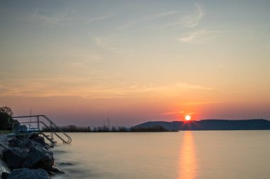 Yazın bir gölün kıyısında gün batımı. Horiont 'u geniş görüşlü, renkli bir gökyüzü. Balaton, Balaton Gölü, Sifok, Macaristan 'da doğa manzarası