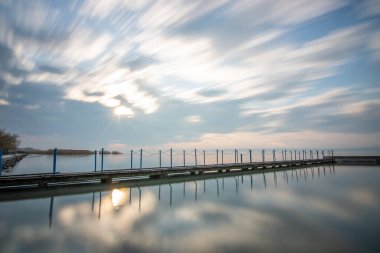 Sakin bir gölün kıyısından alınan su manzarası. Gün batımında ufka yansıyan suyun üzerinden bak. Siofok limanında bir iskele ya da iskele, Balaton, Macaristan