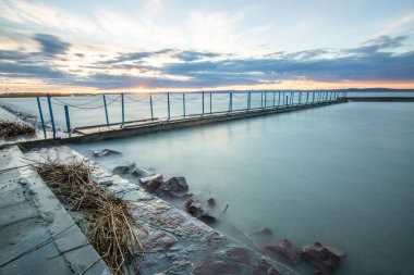 Sakin bir gölün kıyısından alınan su manzarası. Gün batımında ufka yansıyan suyun üzerinden bak. Siofok limanında bir iskele ya da iskele, Balaton, Macaristan