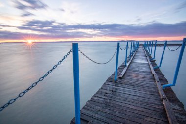 Sakin bir gölün kıyısından alınan su manzarası. Gün batımında ufka yansıyan suyun üzerinden bak. Siofok limanında bir iskele ya da iskele, Balaton, Macaristan