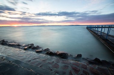 Sakin bir gölün kıyısından alınan su manzarası. Gün batımında ufka yansıyan suyun üzerinden bak. Siofok limanında bir iskele ya da iskele, Balaton, Macaristan