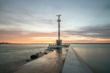 a small marina on a lake. Breakwater and pillar with golden figure in the dreamy sunset. Landscape shot in Sifok, Balaton, Hungary clipart