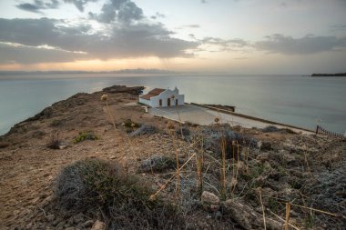 Yunanistan 'ın tipik mimari tarzında küçük beyaz bir kilise. Akdeniz ve güneşin doğuşuyla çevrili bir ağacın üzerinde duruyor. Agios Nikolaos Şapeli, İyon Adaları, Yunanistan