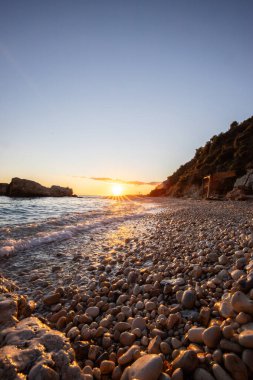 Gün doğumunda gizli körfez. Küçük kuma, çakıl taşına, sıcak renklerde plaja ve sabah ışığına baktım. Xigia Sülfür Plajları 'ndaki deniz manzarası, İyon Adaları, Yunanistan