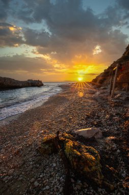 Gün doğumunda gizli körfez. Küçük kuma, çakıl taşına, sıcak renklerde plaja ve sabah ışığına baktım. Xigia Sülfür Plajları 'ndaki deniz manzarası, İyon Adaları, Yunanistan